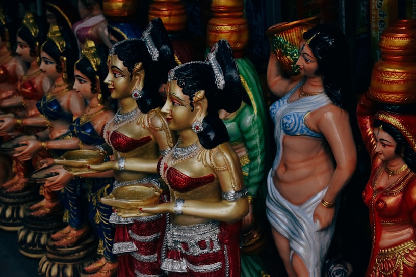 A colorful display of intricately detailed figurines, each dressed in elaborate traditional attire. The figures hold various objects, with vibrant colors and ornate decorations covering their surfaces. They stand in close proximity, suggesting a sense of unity and cultural significance.