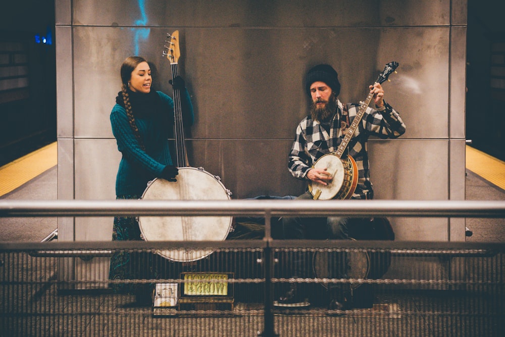 man and woman playing string instruments standing near wall