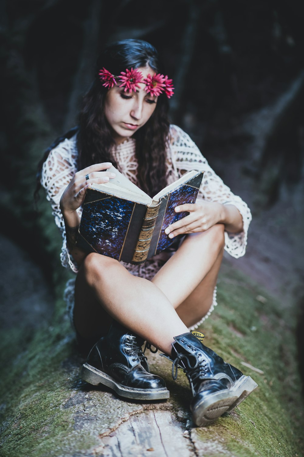 woman wearing white long-sleeved blouse and black leather work boots reading blue and brown book