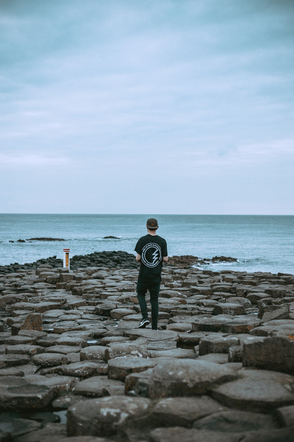 黒いシャツとズボンを着た男が、水辺の灰色の岩の上を歩いている