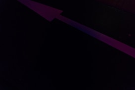 A dark background with a prominent large pink arrow pointing upwards, possibly on a road or floor.