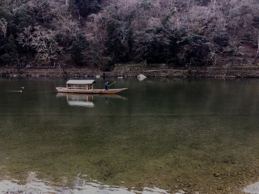 person riding boat on body of water beside trees