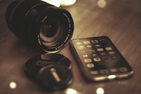 Close-up of a camera lens and smartphone on a stylish desk with soft lighting.