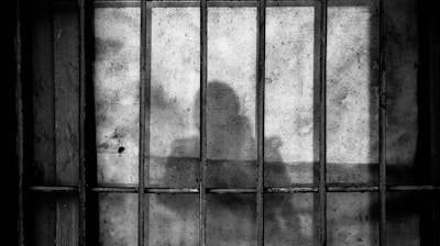 a shadow of a person behind bars in a jail cell