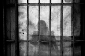 a shadow of a person behind bars in a jail cell