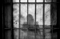a shadow of a person behind bars in a jail cell