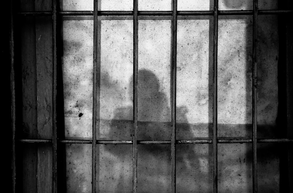 uma sombra de uma pessoa atrás das grades em uma cela de prisão