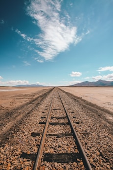 brown train rail in desert under blue and white sky