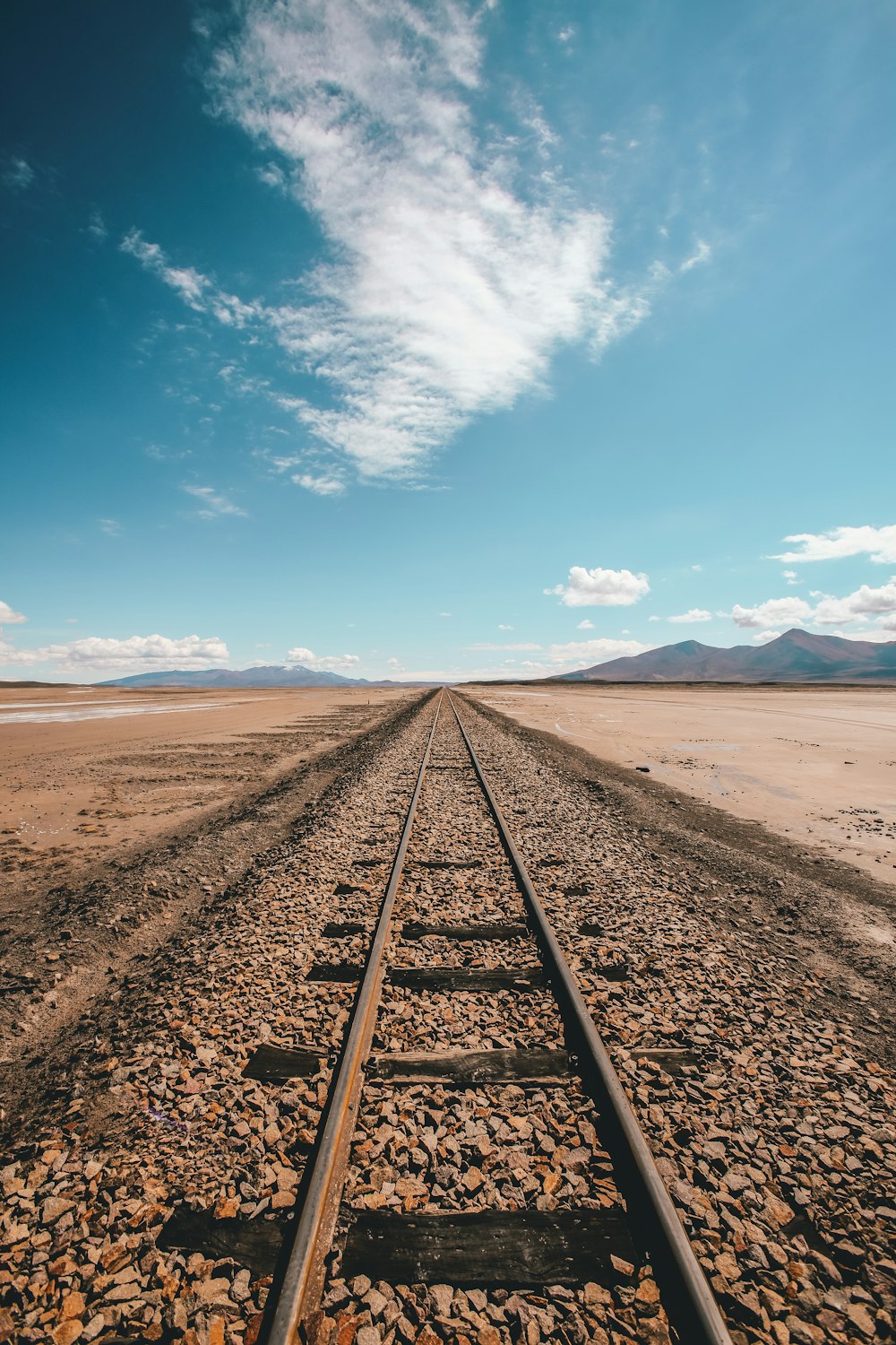 青と白の空の下、砂漠に浮かぶ茶色の列車のレール