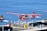 A seaplane with a red and white design featuring a maple leaf is parked at a dock on a calm body of water. The aircraft is labeled with 'HARBOUR AIR' and 'CANADA 150.' Other seaplanes are visible in the background, along with dock equipment such as barrels and crates. The overall setting appears to be a seaplane terminal or harbor.