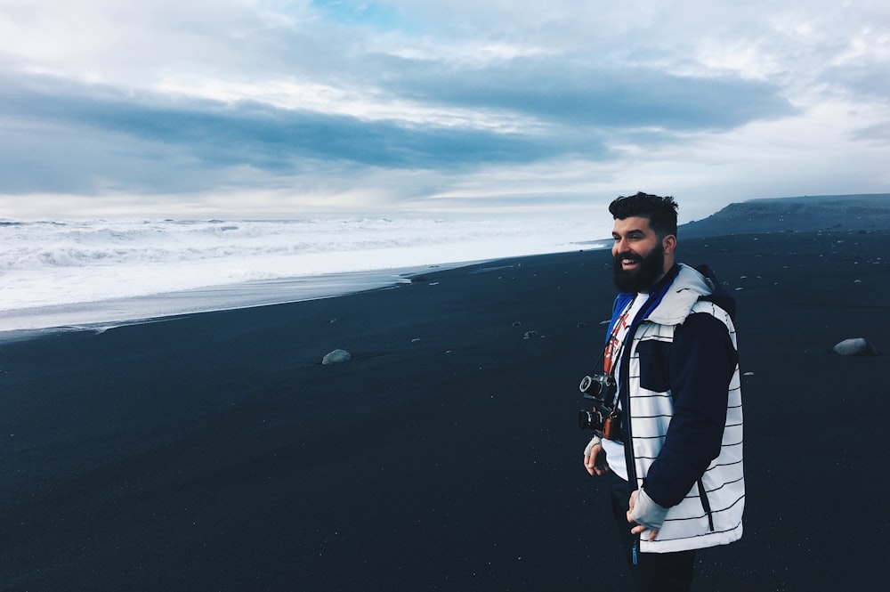 man carrying black DSLR camera standing near sea