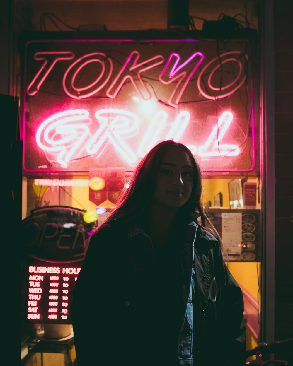 woman standing behind red Tokyo Grill neon signage