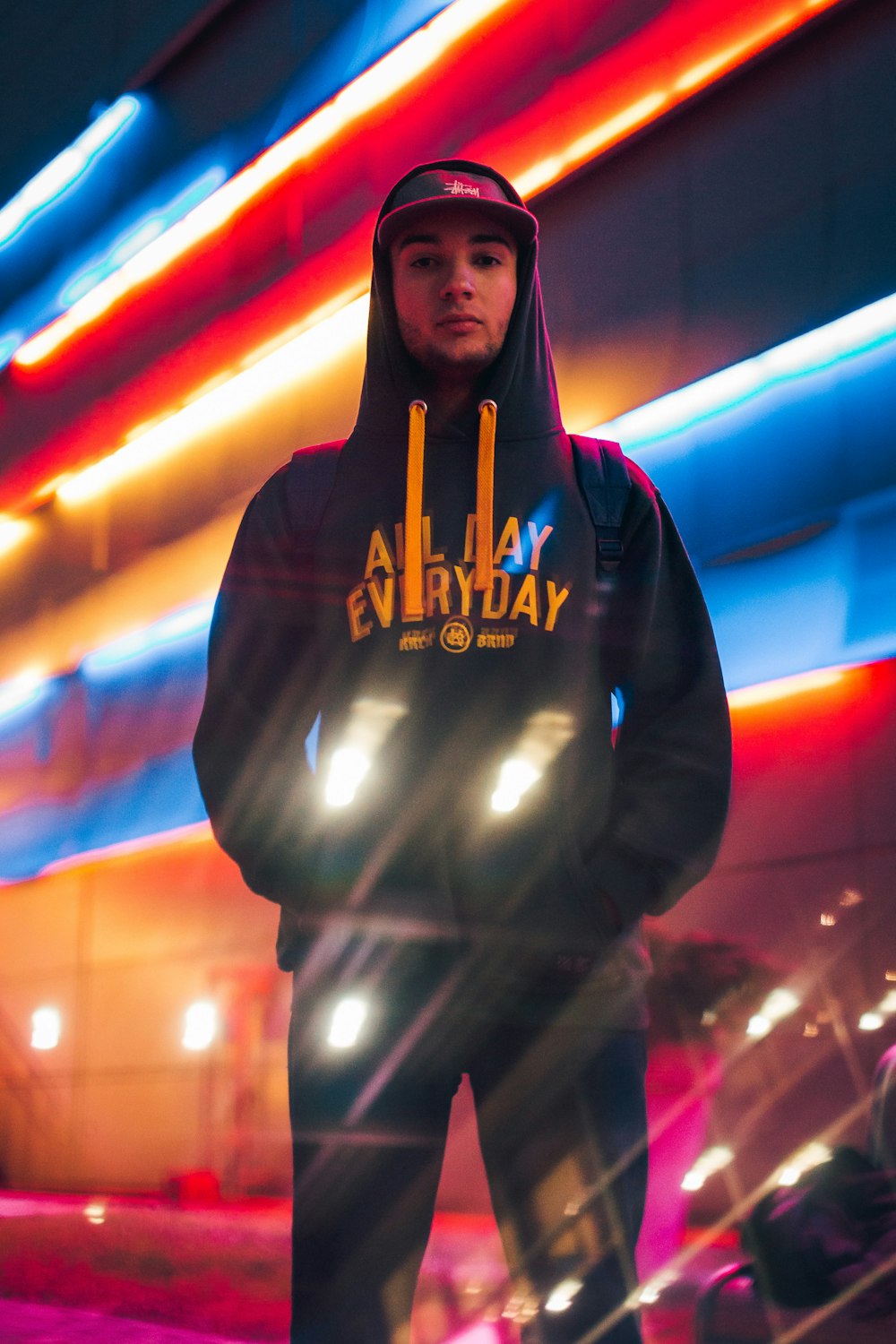 man standing behind building with red and blue neon lights