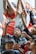 A group of children are enthusiastically raising their hands and making expressive faces, possibly during a game or an interactive activity. The scene is lively and crowded, with the children wearing colorful clothes. There is a sense of movement and excitement among the group.