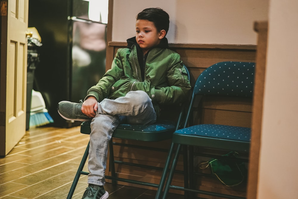 boy in green jacket sits on folding padded chair near door inside room