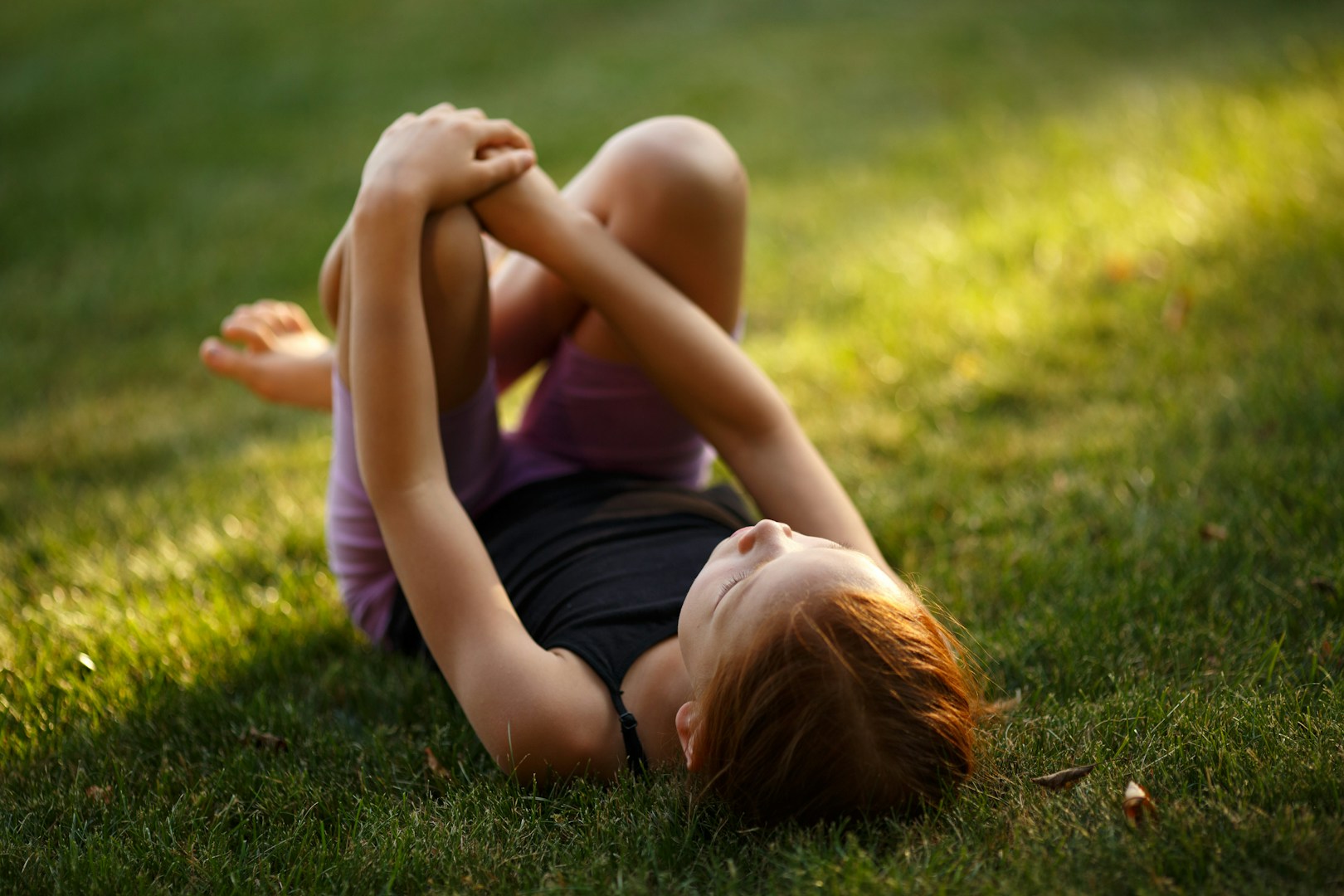 young girl laying on her back on the grass with legs folded up