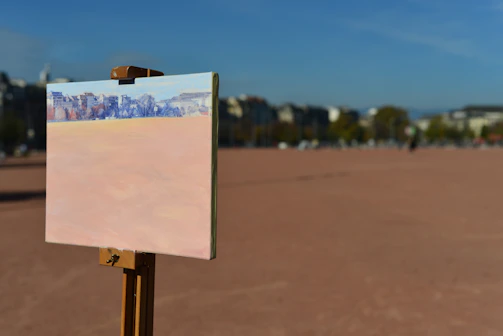 Artist working on a large canvas outdoors with city skyline in background.
