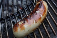 Grilled longaniza sausage on the grill with smoke rising in the background.