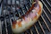 Close-up of a sizzling Carolina sausage link topped with grilled onions and peppers on a toasted bun.