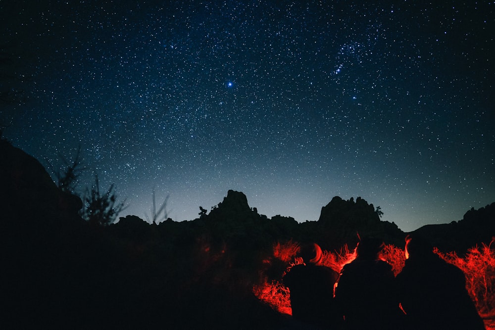 silhouette photo of three person sitting infront of bonfire under night sky