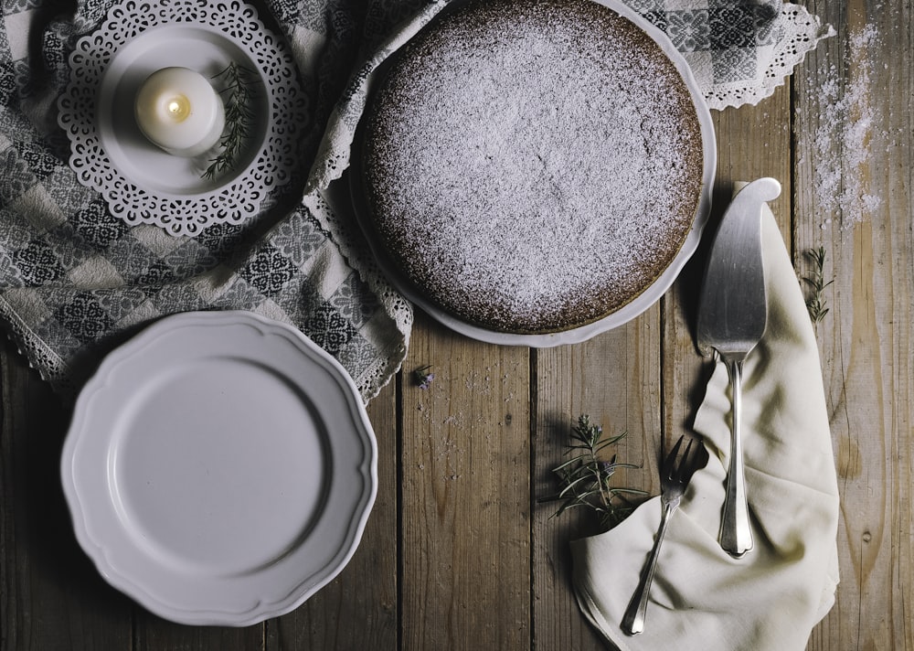 Pastel en plato de cerámica blanca junto a vela candelita blanca y servidor de pasteles