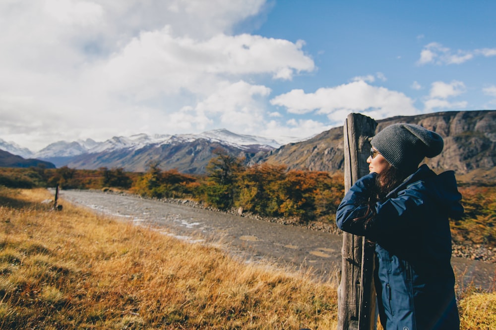 woman wearing blue jacket leaning on brown wooden post