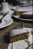 A slice of homemade cake with a dusting of icing sugar, set against a backdrop of the cozy cafe interior.