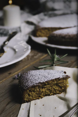 A slice of homemade cake with a dusting of icing sugar, set against a backdrop of the cozy cafe interior.