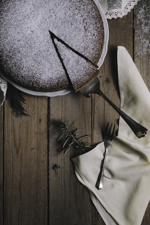 A freshly baked golden cake with powdered sugar dusted on top, sitting on a rustic wooden table.