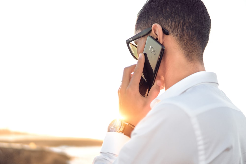 uomo che tiene lo smartphone in piedi davanti allo specchio d'acqua calmo