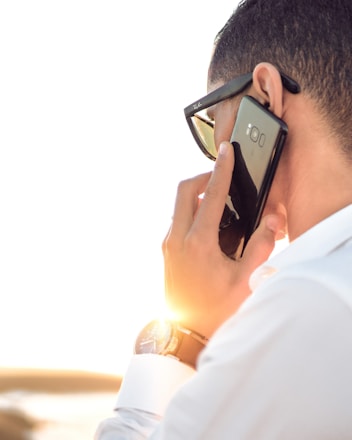 man holding smartphone standing in front of calm body of water