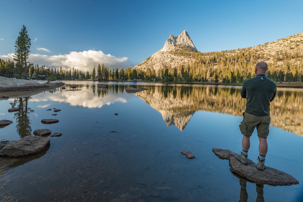 man standing near rock between body of water during daytime