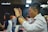 A group of people appear engaged in an activity that involves raising hands. The central person in focus is a man with short hair, wearing a white shirt and a black wristwatch, seemingly in concentration or worship.