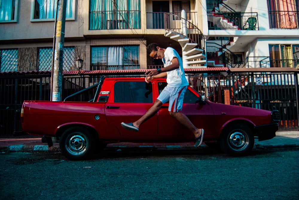 man jumping beside red pickup truck