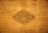 An intricate wooden carving with floral and leaf patterns centered against a distressed wooden panel background. The carving displays detailed craftsmanship with symmetrical designs radiating from a central floral motif.