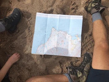 Close-up of trekking boots and a map laid out on a forest trail.