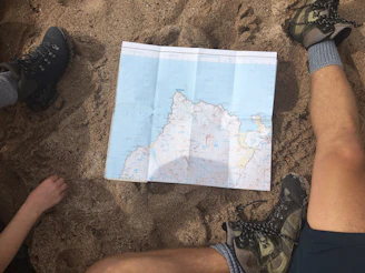 Close-up of trekking boots and a map laid out on a forest trail.