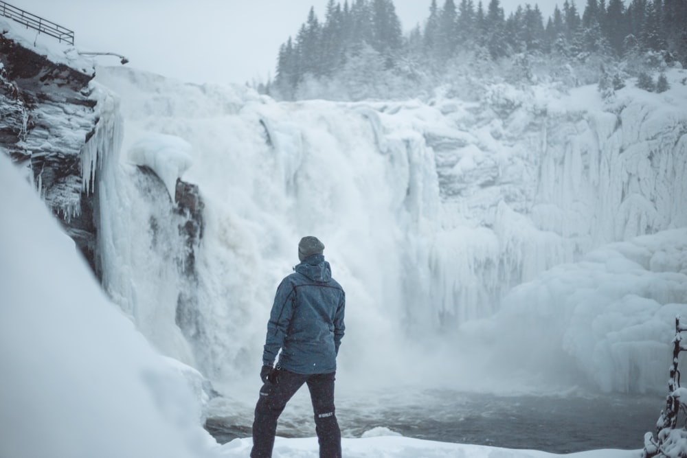 man standing near snow covered falls during daytime