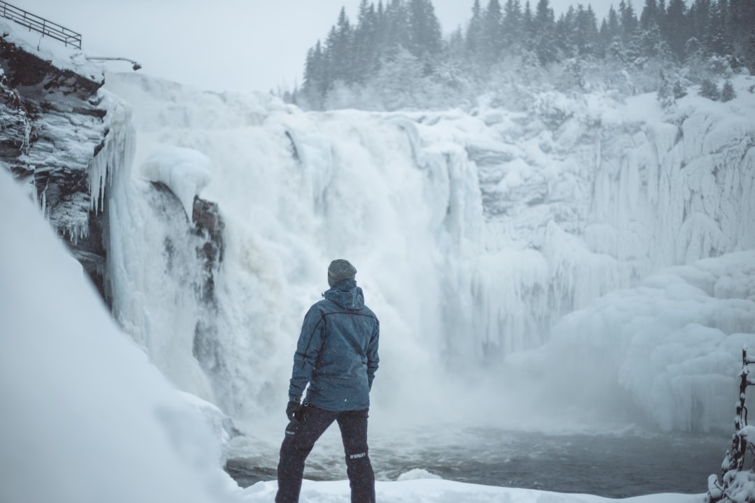 man standing near snow covered falls during daytime