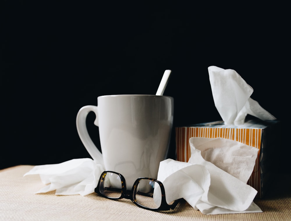 white ceramic mug on white table beside black eyeglasses