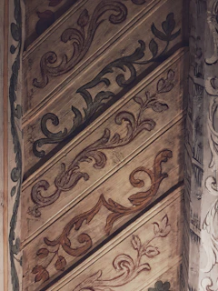 Brightly painted wooden panel with whimsical leaf patterns blending into the wood's knots.