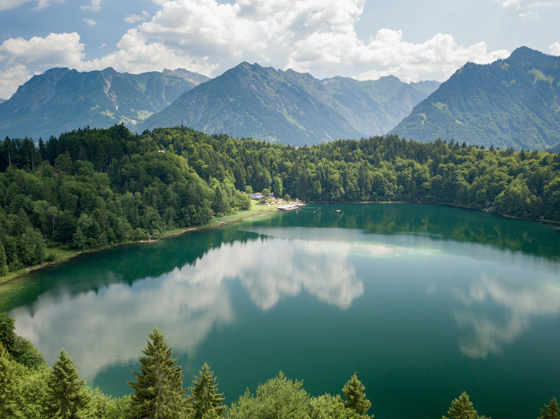 green forest near lake and mountain under cloudy sky