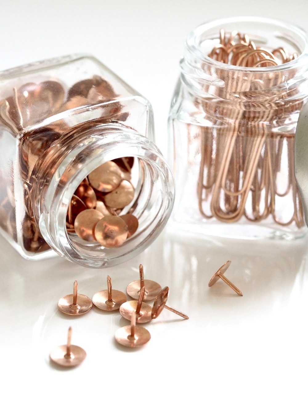 photo of bronze-colored thumb tacks and paper clips in clear glass bottles