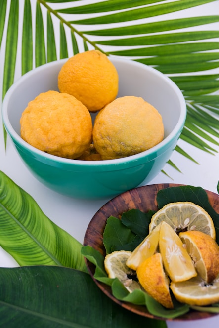 A vibrant glass of fresh lemon juice surrounded by whole lemons and green leaves on a rustic wooden table