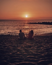 man and woman sitting on beach during golden hour