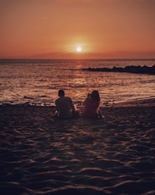 man and woman sitting on beach during golden hour