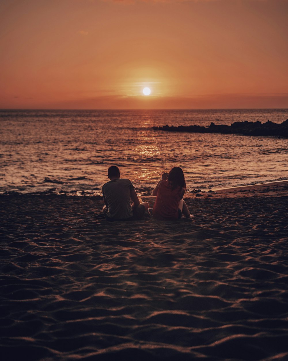 man and woman sitting on beach during golden hour