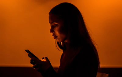 A warm, inviting photo of a woman using a smartphone app in a cozy, softly lit room.