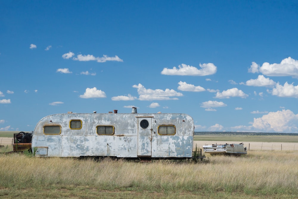 gray metal travel camper on grass land under blue and white cloudy skies at daytime