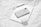 An arrangement of Apple products including a smartphone, tablet, wireless earbuds case, and a stylus on a textured white paper background. The devices are neatly placed, showcasing a sleek and modern design with a minimalist aesthetic.